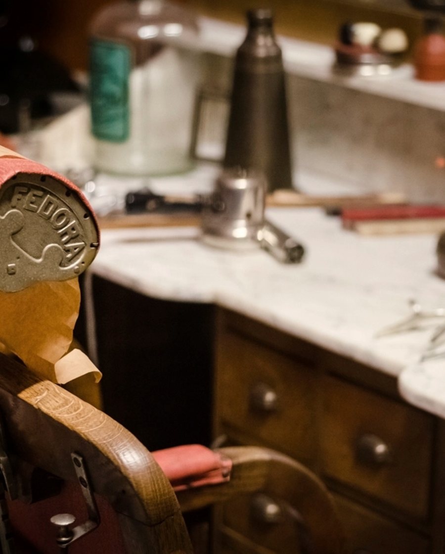 A vintage barber chair headrest in worn leather, with the counter and tools behind it.